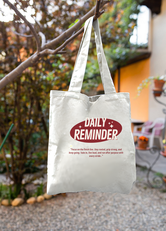 White tote bag with 'Daily Reminder' text hanging outdoors.